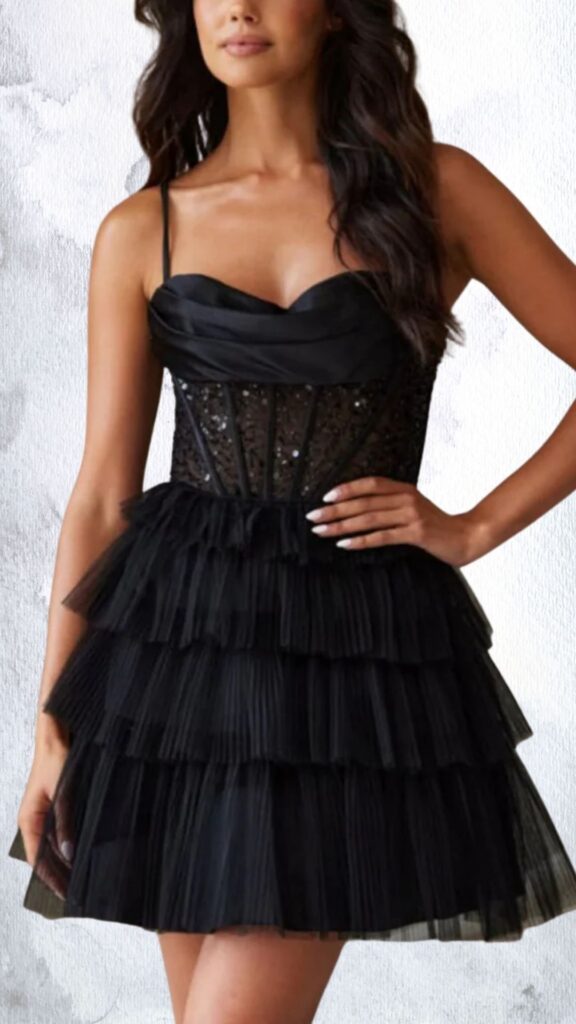 A black mini dress featuring a fitted bodice with a sweetheart neckline and embellished with sparkling beads, transitioning into a playful layered pleated skirt. The dress has thin adjustable straps and a flared hemline that ends mid-thigh, adding a flirty touch to its elegant silhouette. The textured detailing of the bodice contrasts with the soft layers of the skirt, creating a striking visual effect.