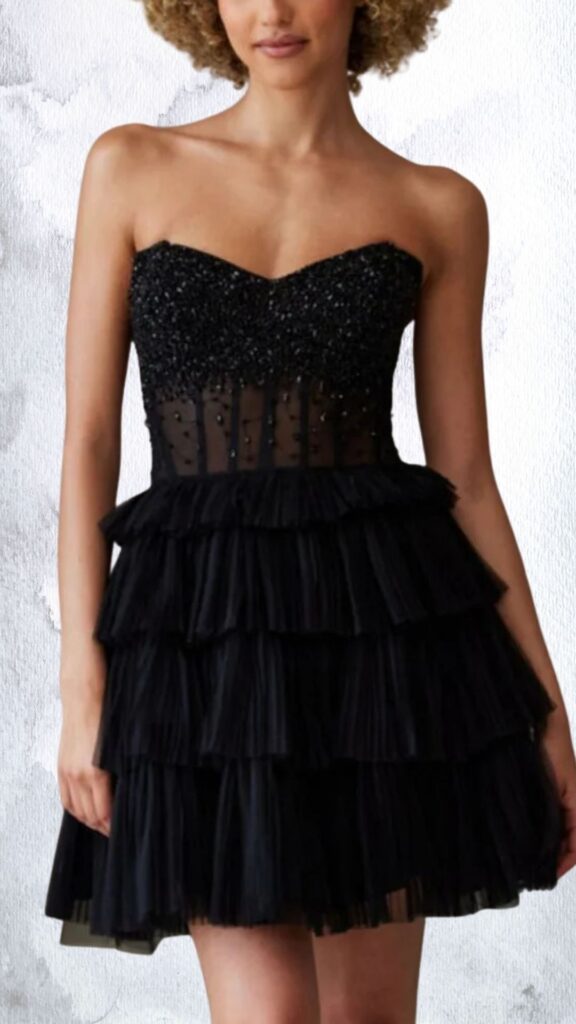 The dress features a fitted, strapless silhouette with a sweetheart neckline, adorned with intricate beadwork and sequins on the bodice. Below, it transitions into a flared skirt composed of multiple layered ruffles, providing movement and texture, with a high-low hemline that enhances its playful design. The combination of sheer details at the waist and the embellishments creates a chic, glamorous look suitable for formal occasions.