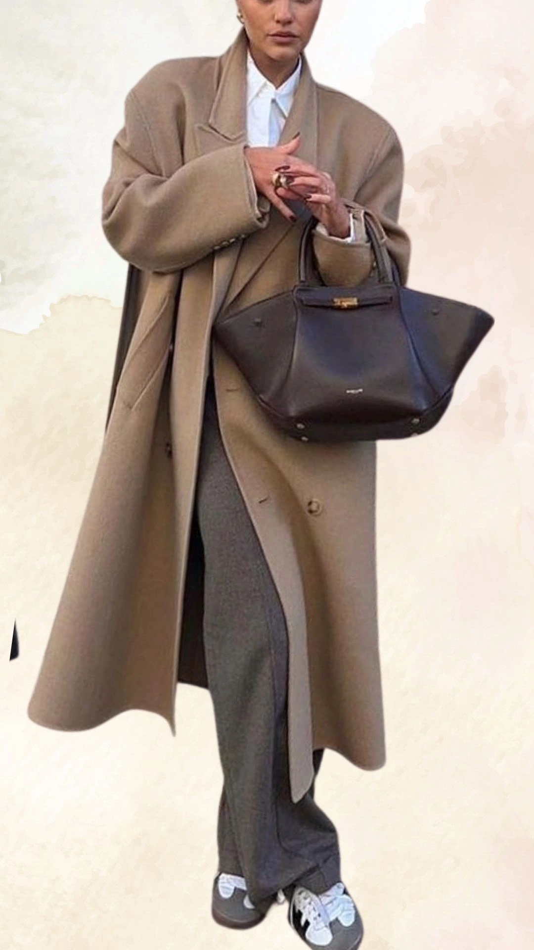 The outfit features an oversized, camel-colored wool coat layered over a crisp white shirt, paired with high-waisted, tailored gray trousers. The look is completed with casual black-and-white sneakers, creating a blend of elegance and comfort suitable for fall. The overall fit of the coat offers a relaxed silhouette, while the tailored trousers provide structured contrast.