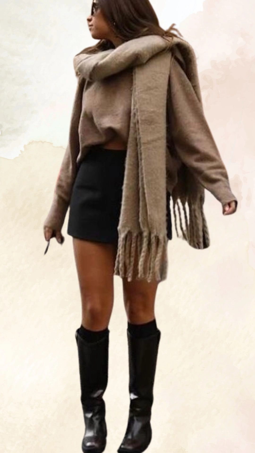 The outfit features an oversized, cropped taupe sweater paired with a high-waisted black mini skirt, creating a balanced silhouette. The sweater has long sleeves with wide openings and a casual, relaxed fit, while the skirt hugs the body, offering a chic contrast. Completing the look are tall, glossy black boots that add an edgy vibe to this casual fall ensemble.