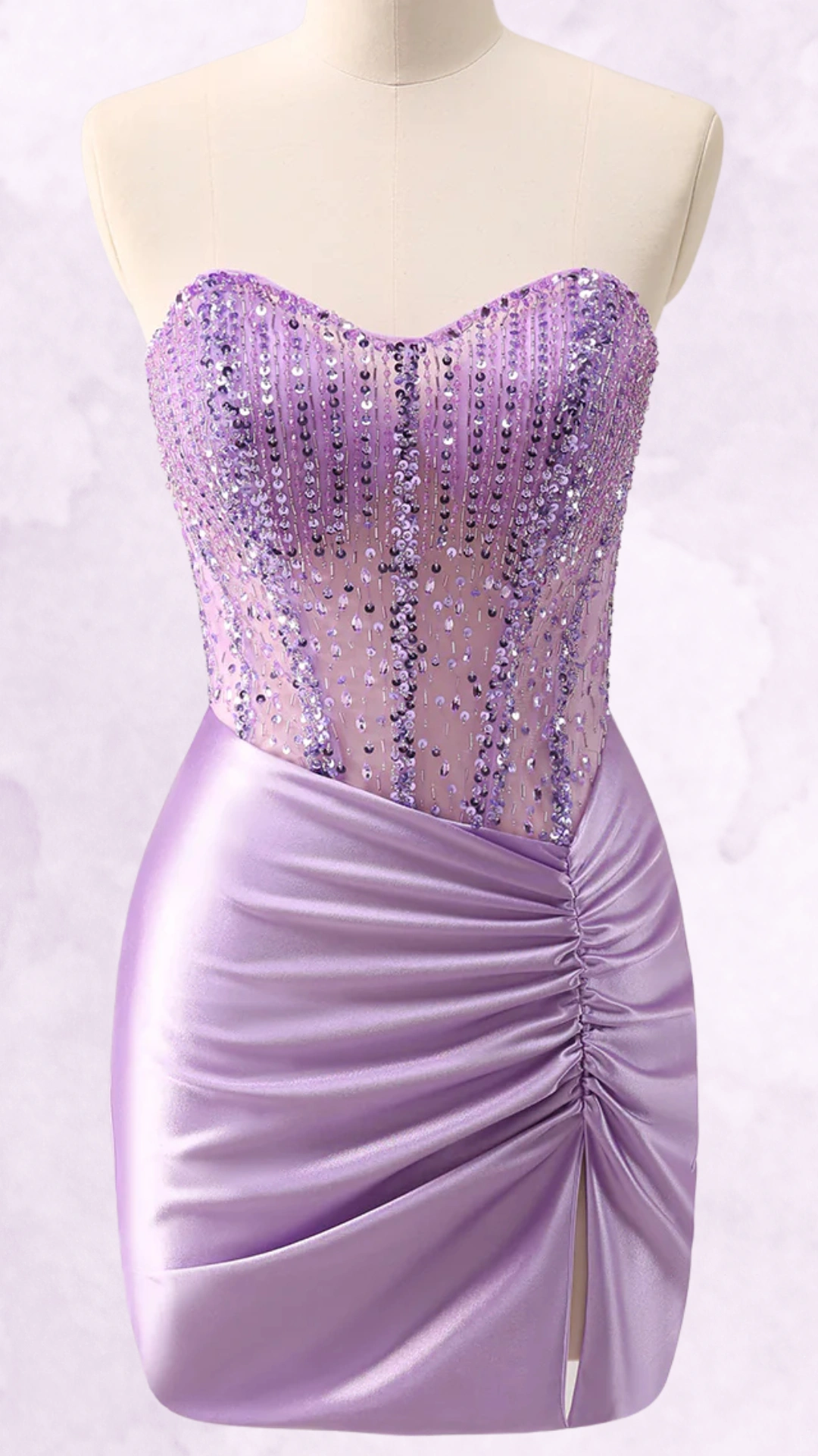 This dazzling homecoming dress features a fitted strapless bodice adorned with shimmering purple sequins, transitioning into a smooth, satin mini skirt with gathered detailing and a side slit. The overall vibe is chic and playful, ideal for a youthful, trendy occasion such as a school dance or party.