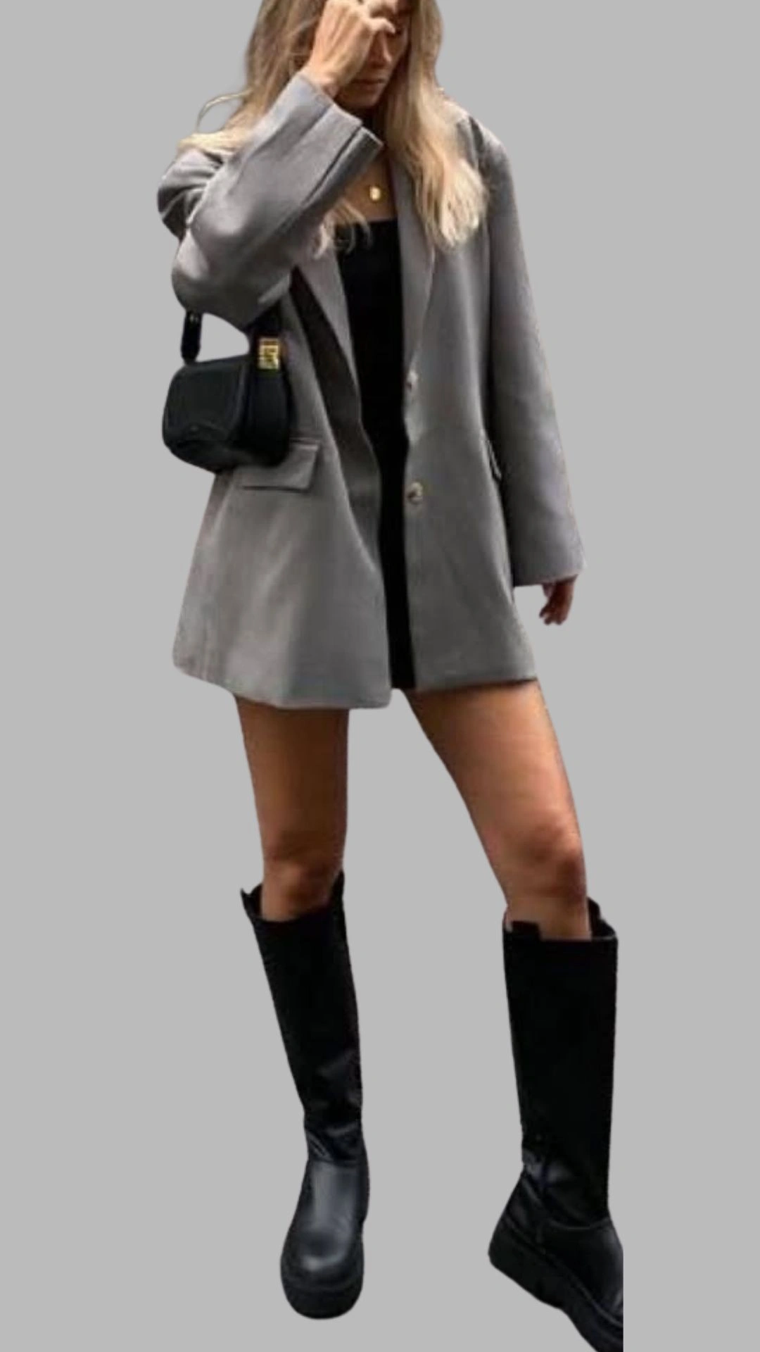 The outfit features a tailored, light grey oversized blazer with a single-button closure and wide sleeves, layered over a sleek black mini dress. Paired with knee-high black boots that have a chunky sole, this ensemble combines a casual yet chic aesthetic, highlighted by the contrasting colors of grey and black. A small black crossbody bag adds a functional detail to the contemporary look.