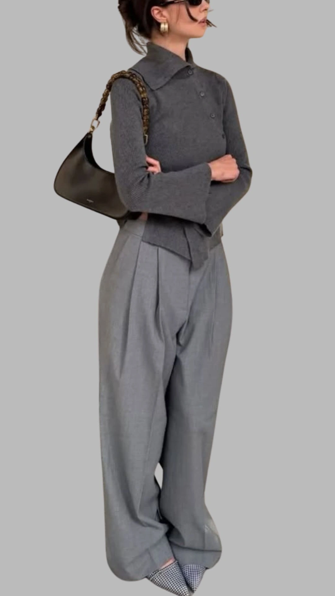 The outfit features a fitted grey, long-sleeve top with a collared neckline and button details. Paired with high-waisted, wide-legged trousers in a light grey fabric, the look is polished yet relaxed, enhanced by a subtle check pattern at the hem. Accessories include a chic black bag with a chain strap, adding sophistication to this contemporary ensemble.