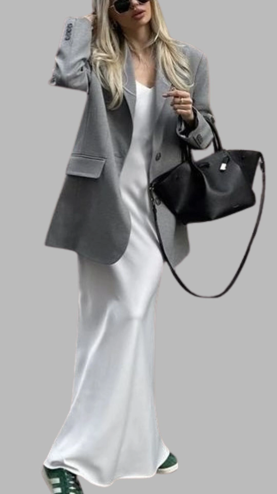 The outfit features a light grey oversized blazer layered over a sleek white slip dress, creating a chic contrast. The dress has a simple, sleeveless design with a relaxed fit that gracefully extends to the floor. Paired with stylish green sneakers, this look combines elegance with casual comfort, making it versatile for various occasions.