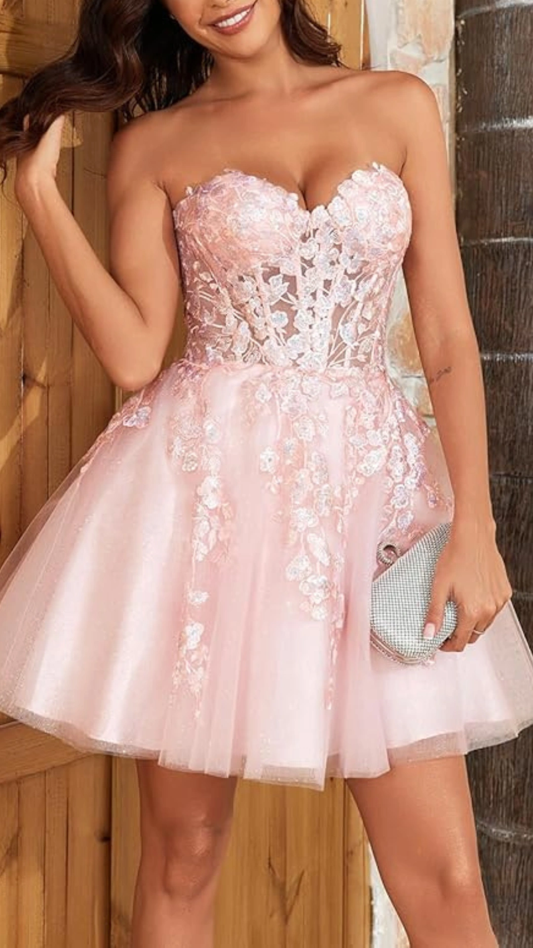 This strapless homecoming dress features a sweetheart neckline and a fitted bodice adorned with delicate floral lace appliqués, transitioning into a flared skirt made from shimmering tulle that adds volume and movement. In a soft pastel pink hue, the overall vibe is romantic and ethereal, making it ideal for formal events and school dances aimed at teenage girls.