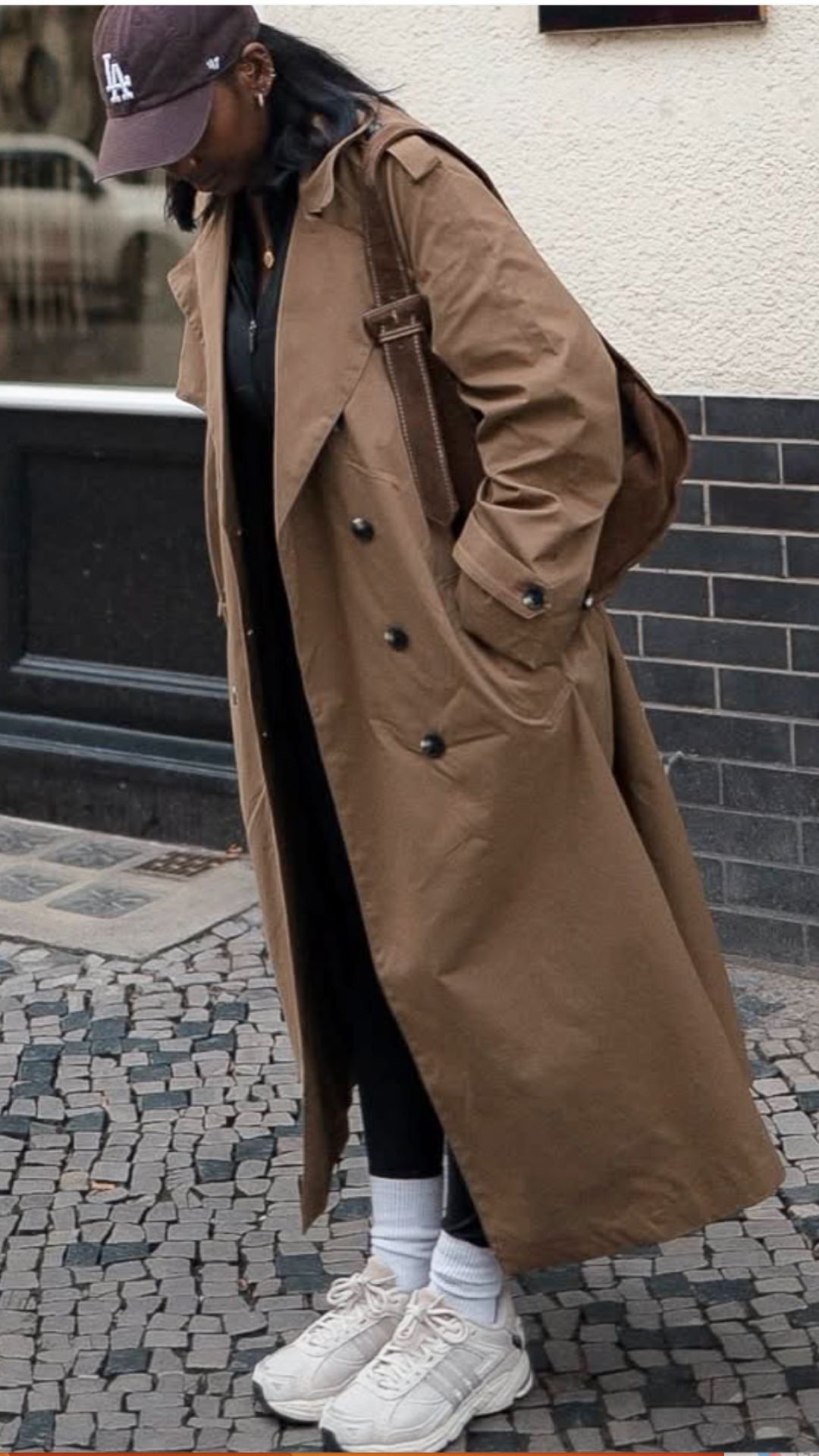 Sporty outfit featuring a relaxed brown trench coat over a black athletic top and fitted black leggings, complemented by white crew socks and chunky white sneakers.