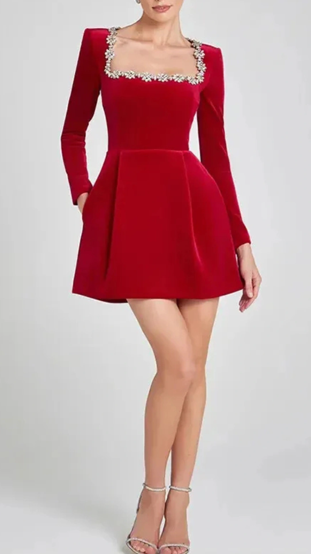 This striking homecoming dress features a vibrant crimson red hue and a soft velvet fabric with a luxurious texture, complemented by long sleeves and a delicate square neckline adorned with floral embellishments. The dress has a fitted bodice that transitions into a playful skirt, creating a flared silhouette that is both trendy and youthful, making it perfect for a festive school dance or formal event for teens.