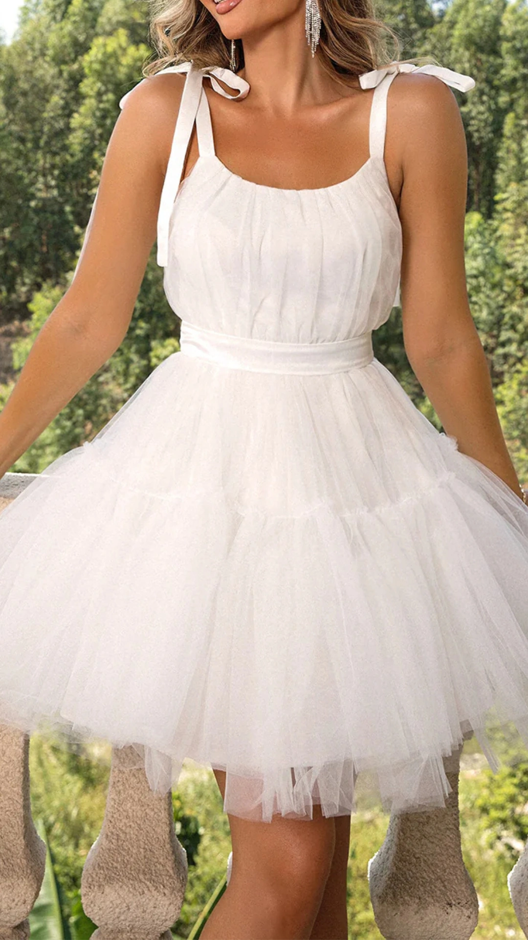 This white homecoming dress features a playful fit-and-flare silhouette with a fitted bodice and a voluminous tulle skirt, creating a whimsical and airy vibe. The fabric has a soft, lightweight texture, complemented by delicate tie straps and a cinched waist that enhances the feminine form, making it an ideal choice for a festive homecoming or school dance.
